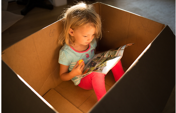 Peschooler girl sitting in box reading a book